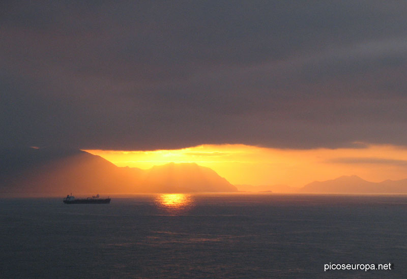 Un buque sale del puerto de Bilbao en la ensenada del Abra, el sol se esconde tras el Pico Candina que preside la ría de Oriñon.
